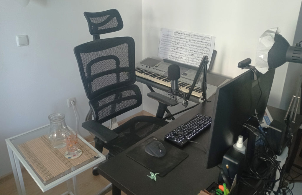 My desk setup, complete a microphone stand, glowy keyboard, a desk lamp converted into a DIY lightbox, and a cameo origami crane