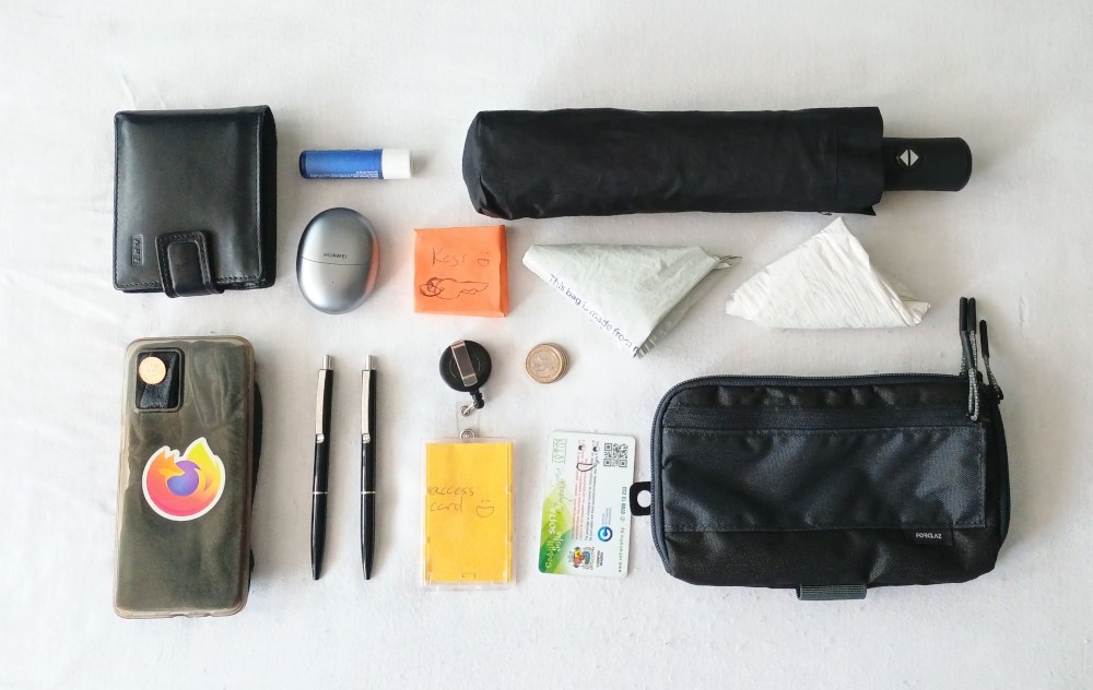 My everyday carry knolled out on a sheet: wallet, lip balm, umbrella (remember the umbrella!), headphones, keys, grocery bags, phone (mocked up with a glove in a case), pens (2!), access card, metro card, loose euro coins, waist bag